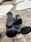 Black thermal rifle scope with LRF, buttons, and lens cap on table, for predator hunting gear