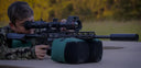 Hunter aiming rifle with thermal scope for predator hunting, using sandbag support in field